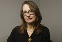 Head shot of Emily Wilson, a white shoulder length brown hair and glasseswoman with