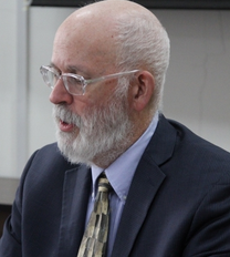 Headshot of Joeseph Farrell, a white man with white hair and beard in a suit